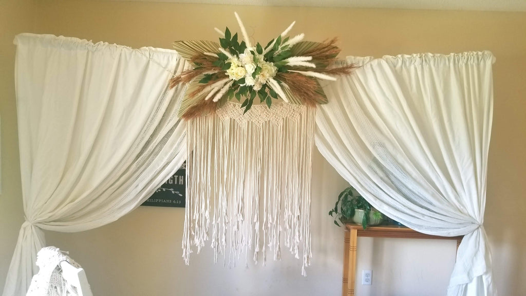 Decorative arch with boho flowers and drapes against a beige wall.