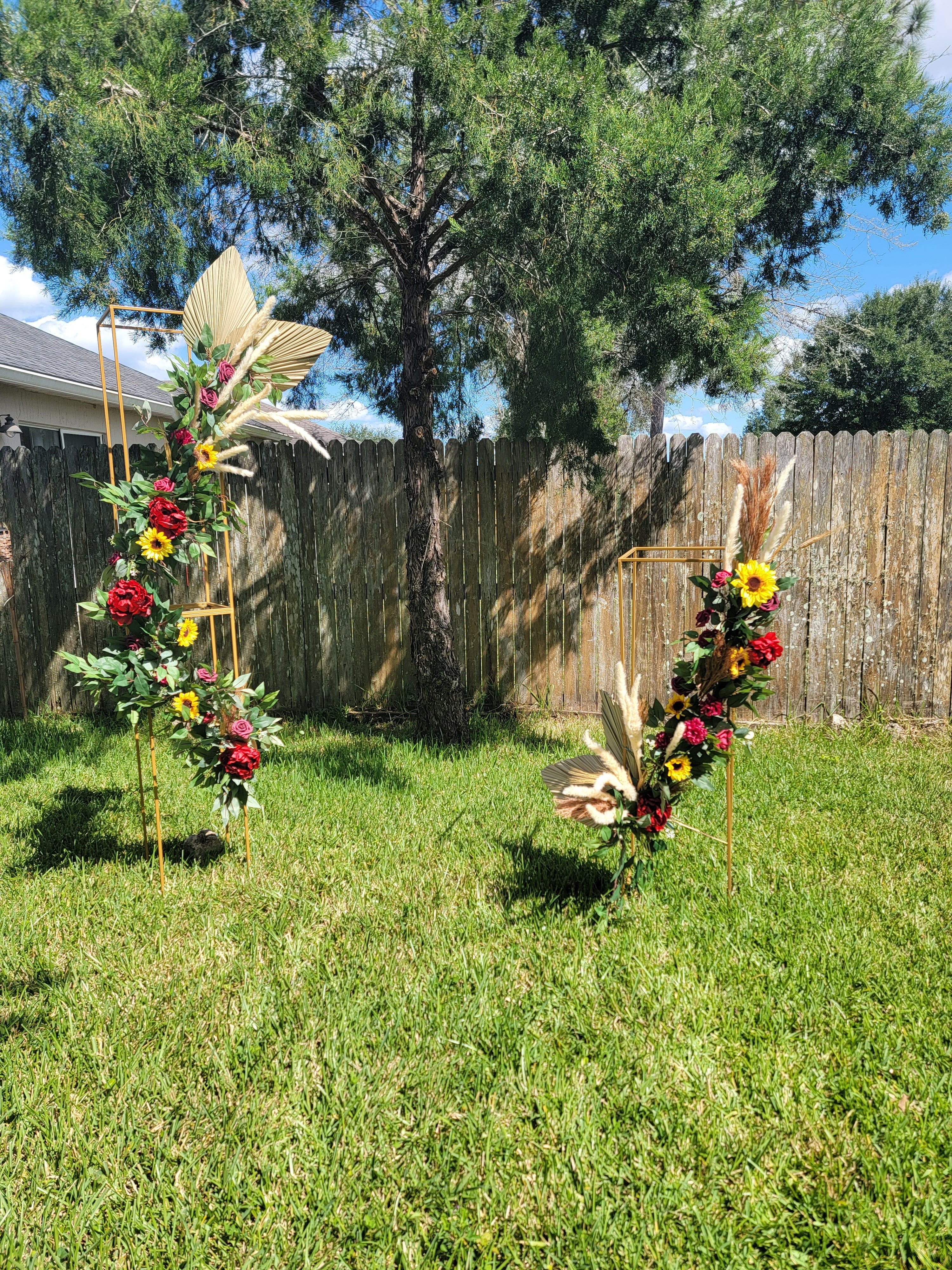 Fall Floral archway decorated with colorful flowers in front of a wooden fence and trees.