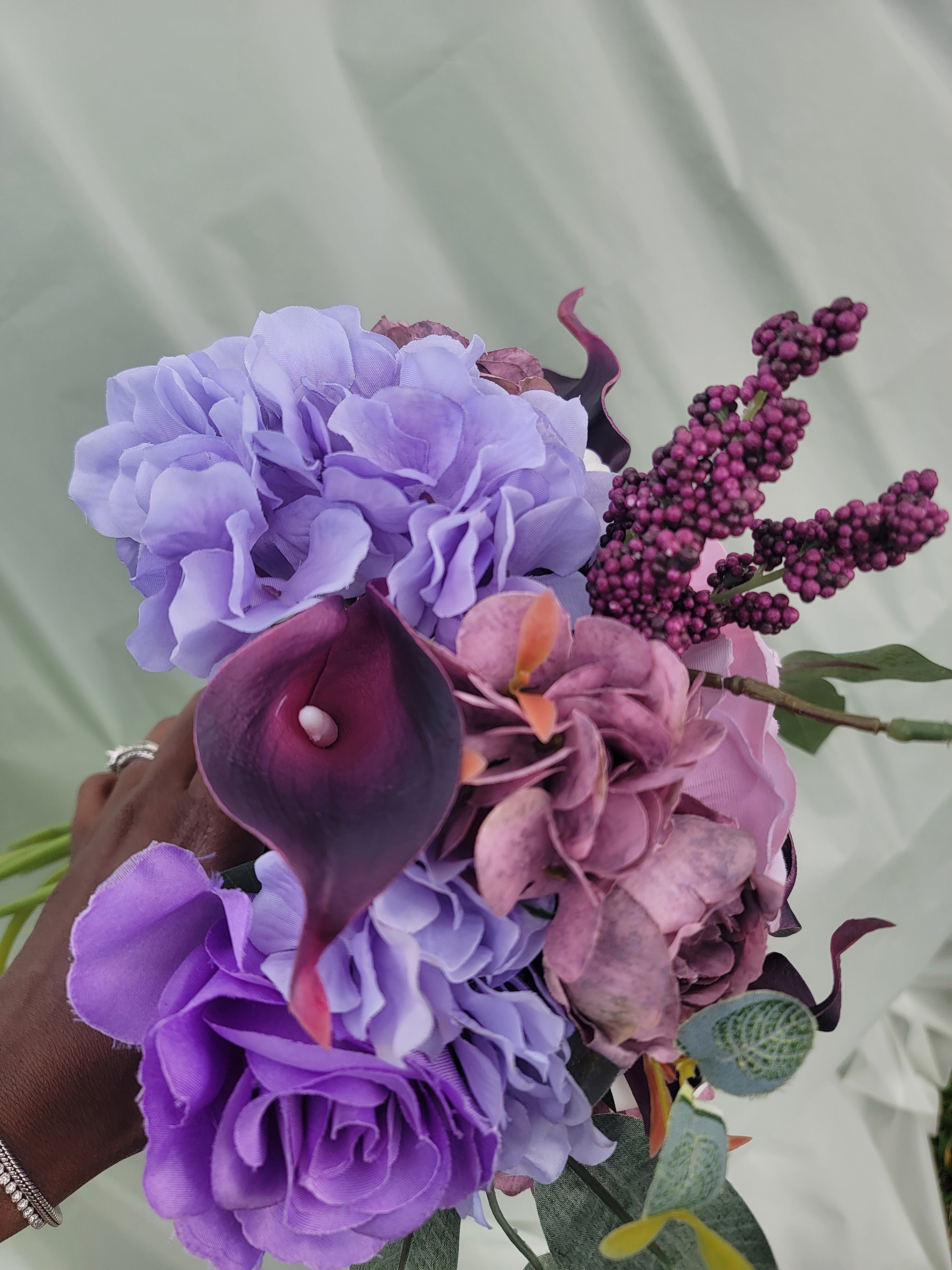 Bouquet of purple and pink flowers held by a hand against a light background