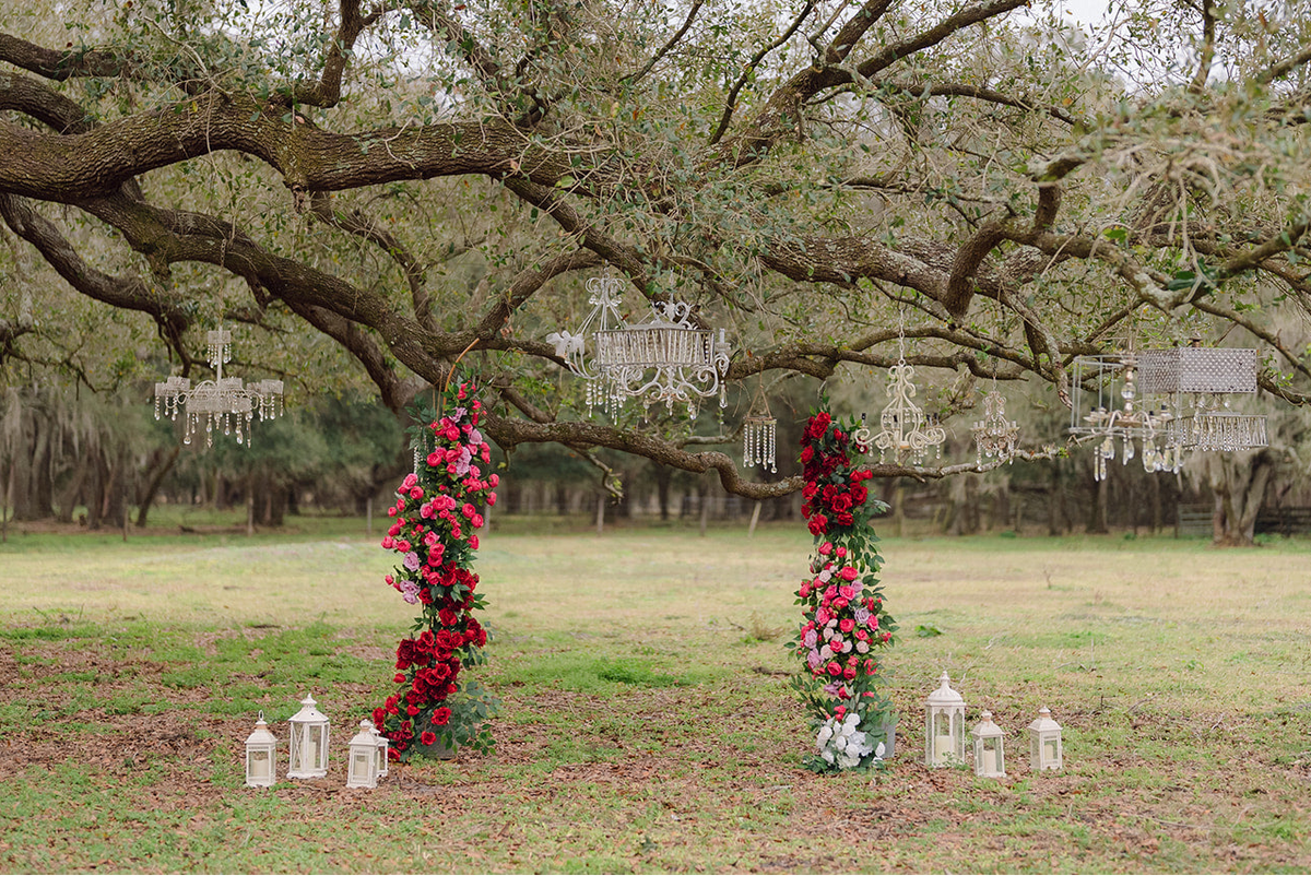 Decorative floral arches with hanging chandeliers and candles in a natural setting.