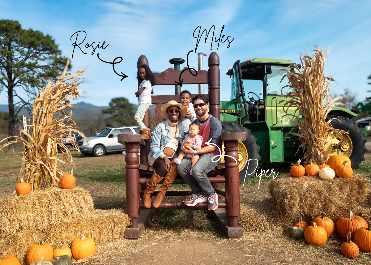 Family sitting on a wooden bench with pumpkins and a tractor in the background