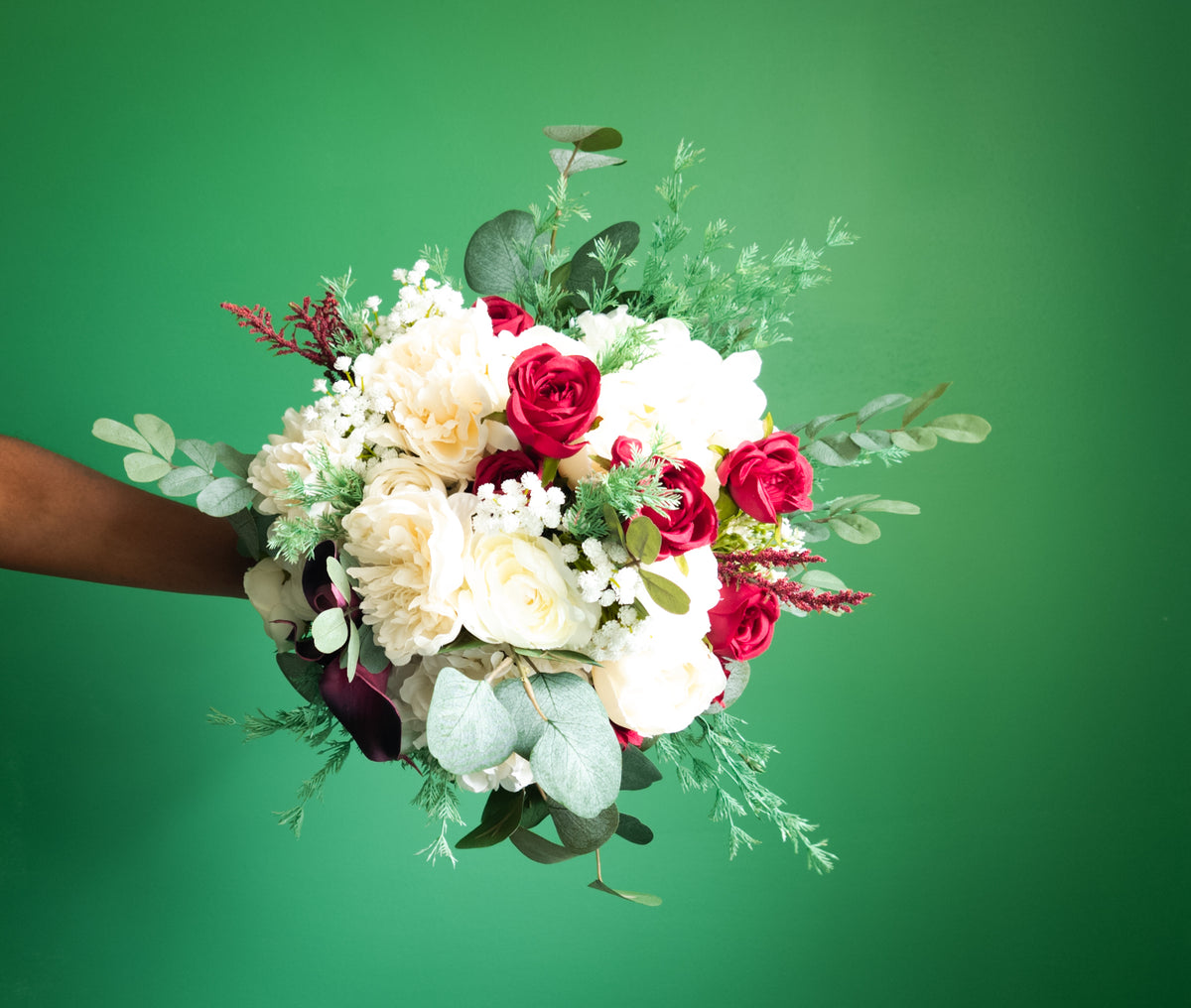 bridal bouquet red and white flowers with greenery held by a person against a green background