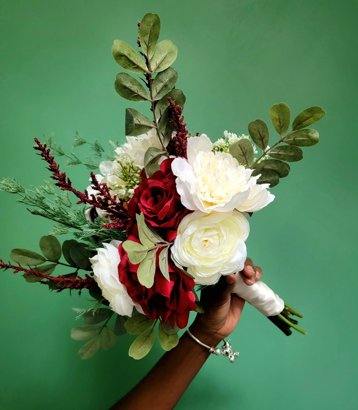 Bridal Bouquet of red and white flowers with green leaves held against a green background - Lynchburg Wedding Flowers