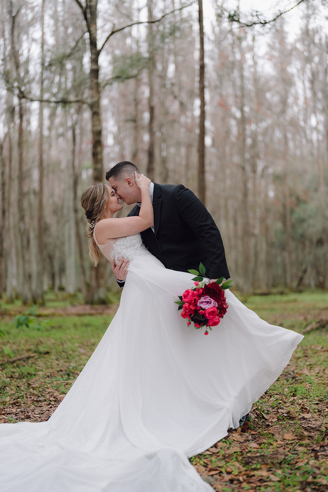 Couple embracing in a forest setting with a bride holding a bouquet.