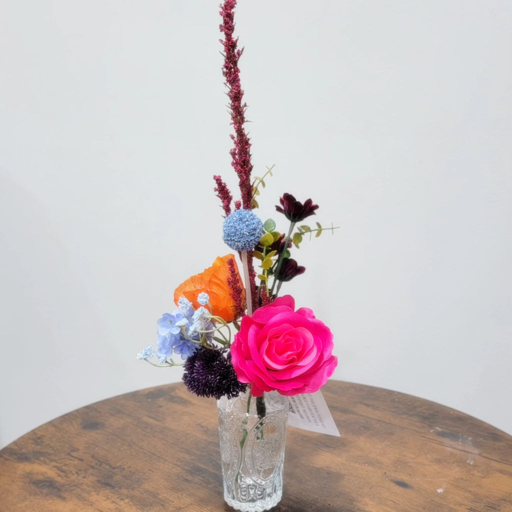Clear glass vase with colorful flowers on a wooden surface against a white background