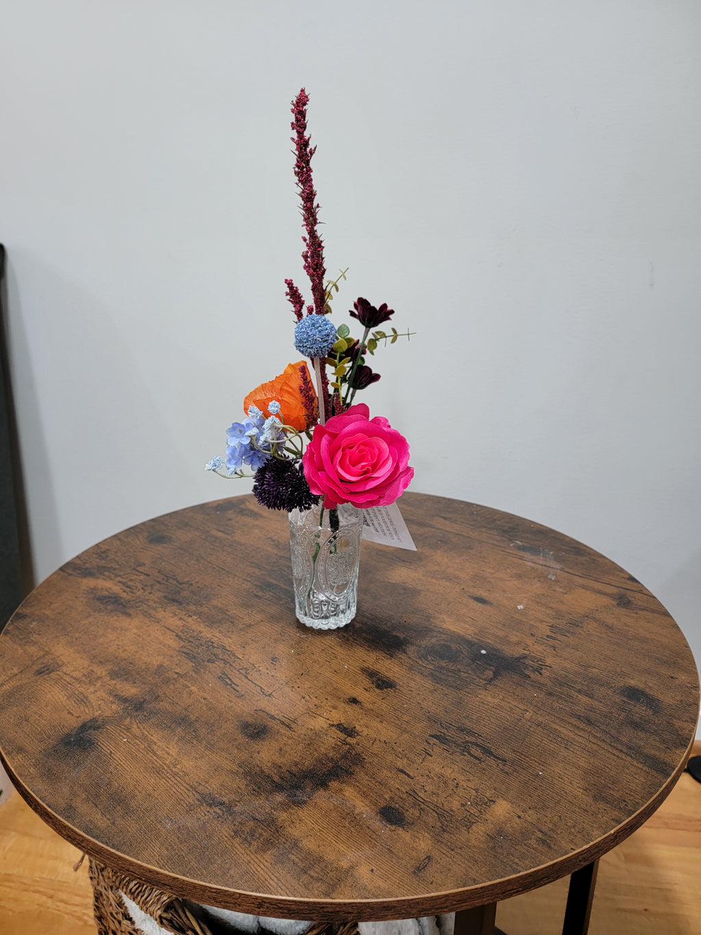 Small bouquet of flowers in a glass vase on a wooden table with a plain background