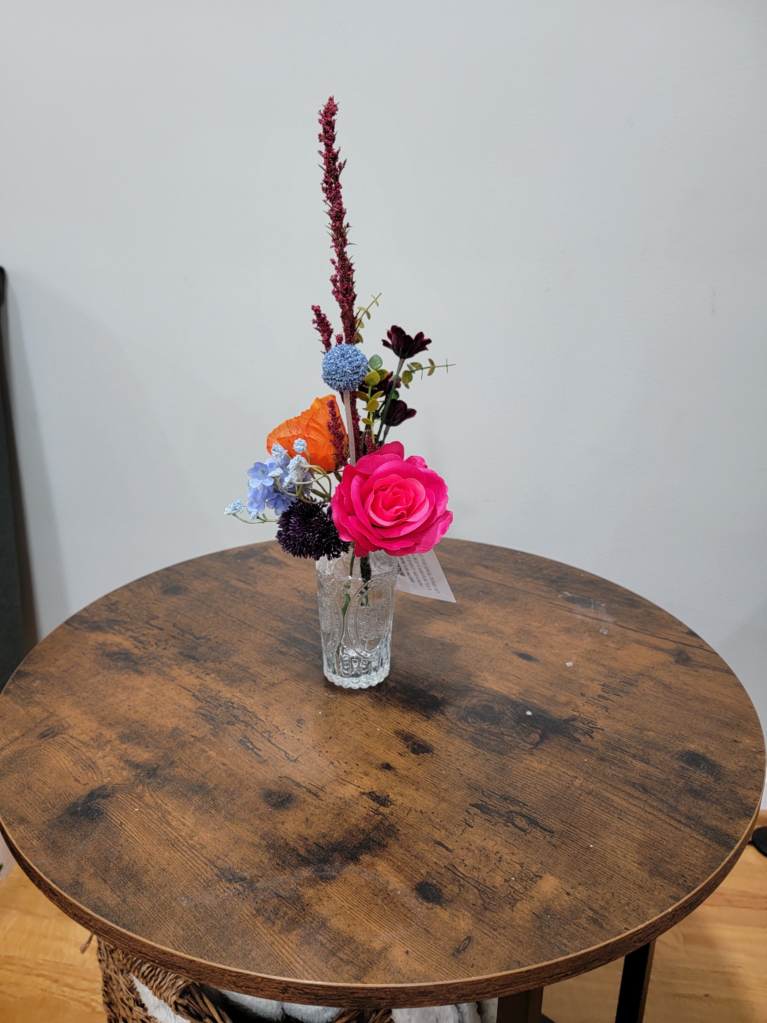 Small bouquet of flowers in a glass vase on a wooden table with a plain background