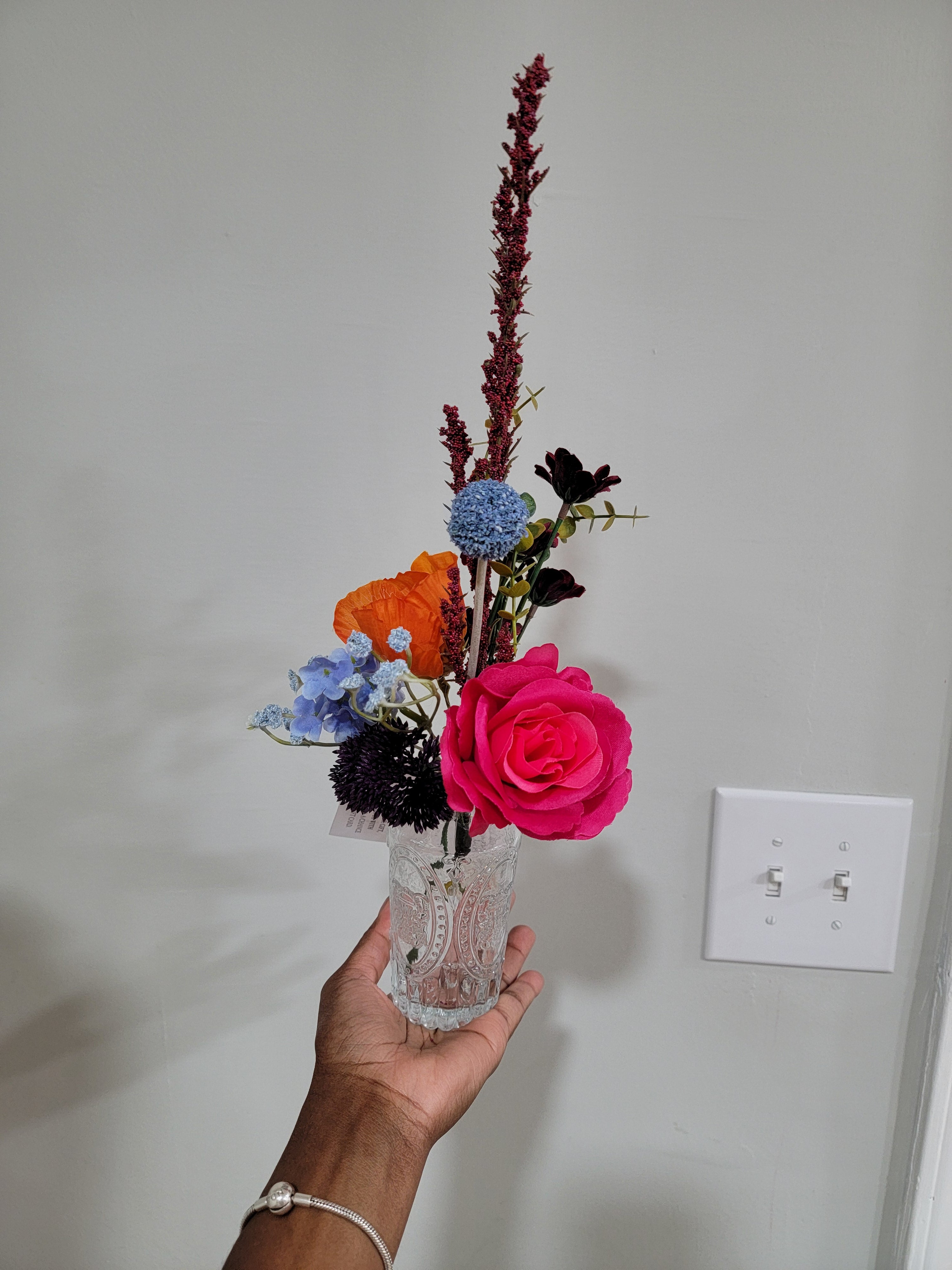 Hand holding a bouquet of flowers in front of a light switch on a white wall